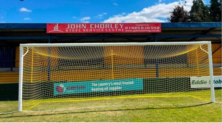 Khán đài phía sau khung thành tại Cantilever Park, sân nhà Warrington Town FC, cho thấy không gian đứng và mái che.